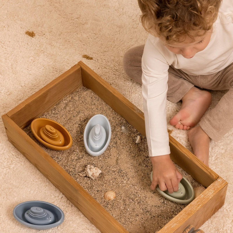 Laad afbeelding in galerijtoner, Een kindje speelt met vier bad bootjes van Little Dutch. De bootjes hebben de kleuren blauw, lichtblauw, groen en okergeel. Het kindje speelt in de zandbak