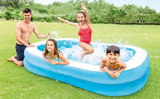 Drie kinderen spelen in een blauw opblaasbaar zwembad van Intex. Een man zit naast het bad en het bad staat op het gras in een achtertuin.