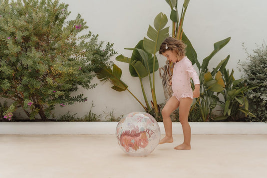 Een meisje speelt buiten met een doorzichtige strandbal van Little Dutch met een roze zeepaardje in de strandbal
