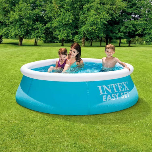 Een moeder, een dochter en een zoontje zwemmen in een blauw rond Intex Easy Set opblaasbaar zwembad. Het zwembad staat op het gras in de achtertuin