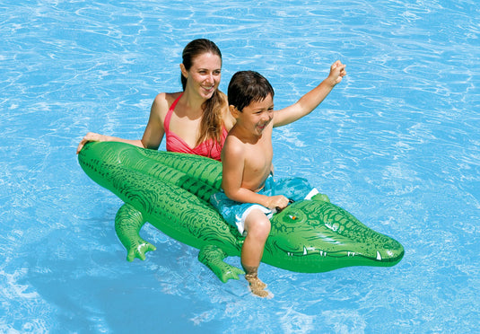 Een vrouw en een kind zwemmen in het water waar het kind zit op een groene opblaasbare krokodil van Intex