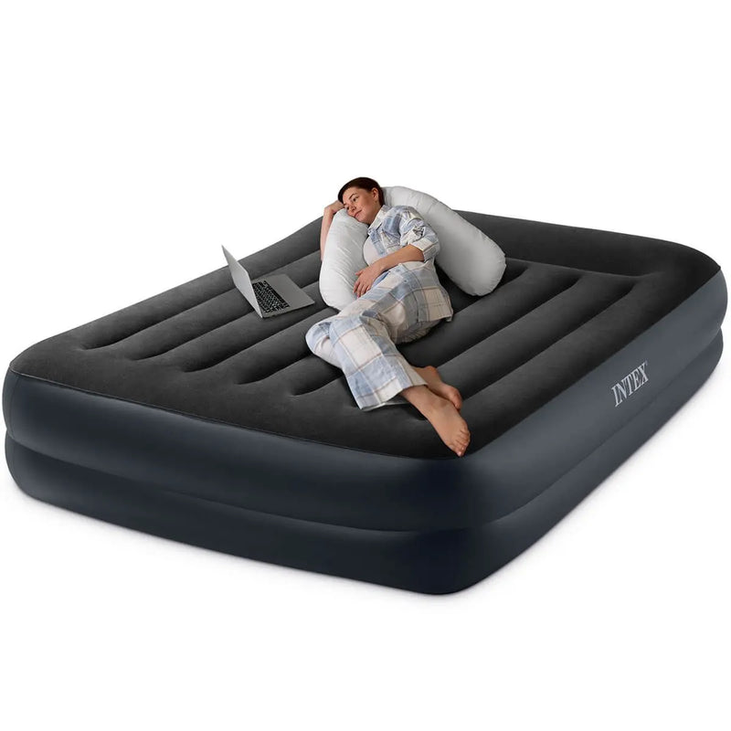 Laad afbeelding in galerijtoner, Een vrouw in pyjama ontspant met haar laptop en kussen op een zwart Intex Pillow Rest Raised Tweepersoons Luchtbed 

