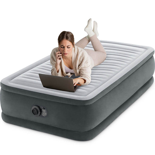 Een vrouw ligt met een laptop op een Grijs Intex Comfort Plush Elevated Eenpersoons Luchtbed