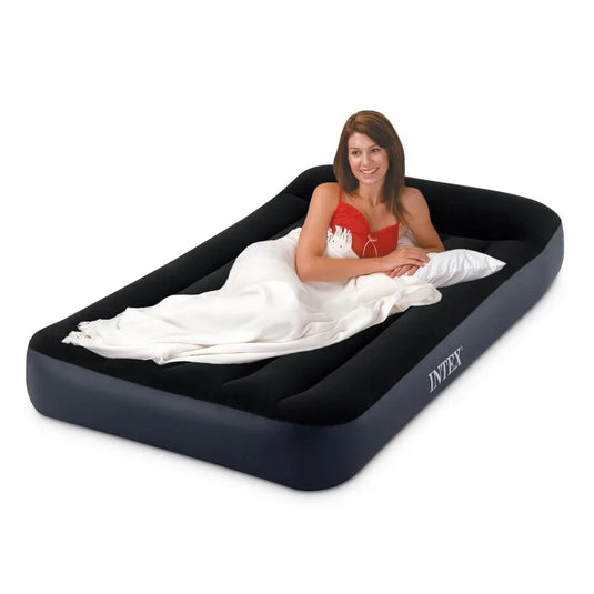 Een vrouw ligt op een zwart Intex Pillow Rest Classic Eenpersoons Luchtbed met een wit kussen en deken.