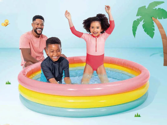 Twee kinderen spelen in een kleurrijk opblaasbaar kinderzwembad van Intex met roze, geel en groene ringen waar een man naast het bad zit