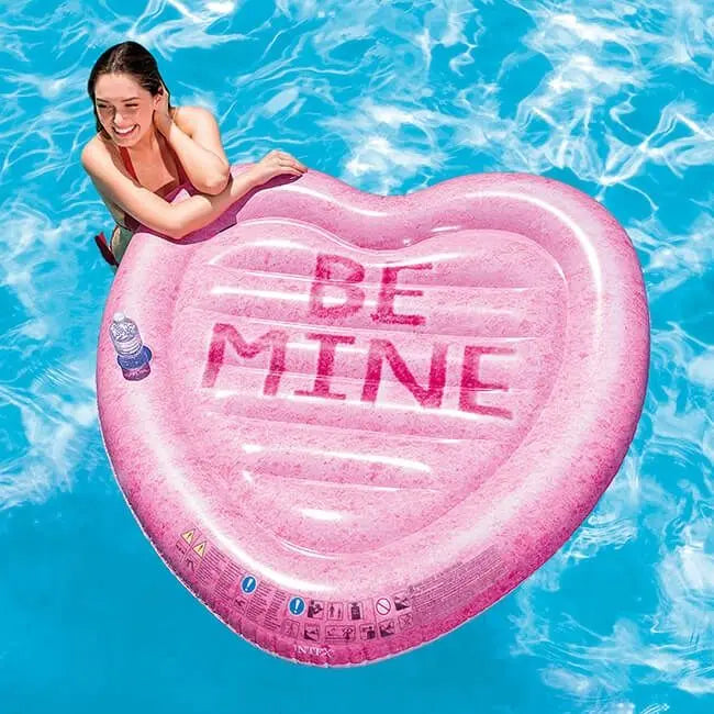 Laad afbeelding in galerijtoner, Een vrouw staat in het water en leunt op een roze opblaasbaar luchtbed van Intex in de vorm van een hartje met de tekst 'BE MINE' 
