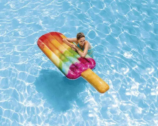 Een vrouw in het water leunt op een regenboog Intex luchtbed in de vorm van een waterijsje