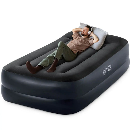 Man geniet van comfortabel slapen op het Intex Pillow Rest Raised Eenpersoons Luchtbed, terwijl hij ontspannen ligt met een wit kussen en koptelefoon.