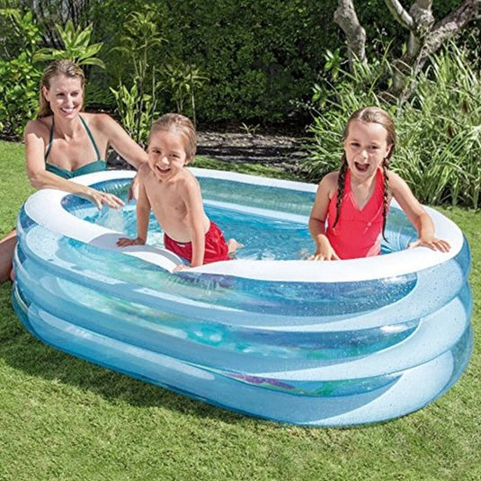 Twee kinderen spelen in een blauw met wit ovalen opblaasbaar Intex zwembad. Het bad staat op groen gras in een achtertuin en hun moeder zit naast het badje