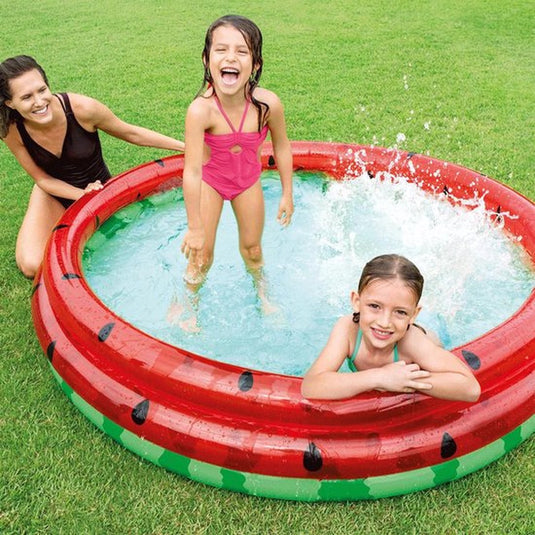 Twee kinderen zwemmen in een rond opblaasbaar zwembad in de stijl van een watermeloen van Intex waar hun moeder naast het bad zit
